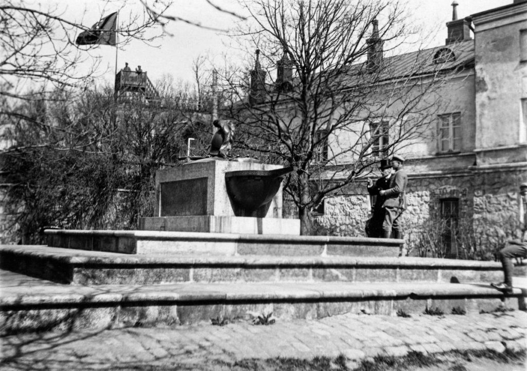 Svartvit bild av Ehrensvärds grav på Slottsgården med Finlands första flagga vajande i bakgrunden. 