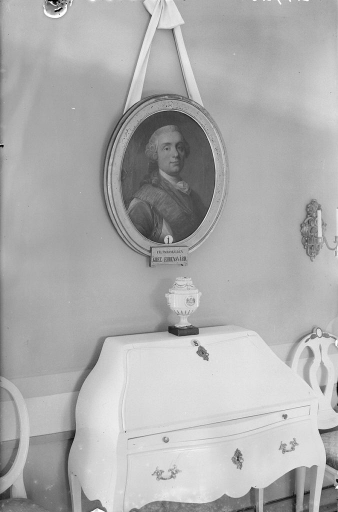 Svartvit bild av interiör med fokus på porträtt av Ehrensvärd hängande på väggen.