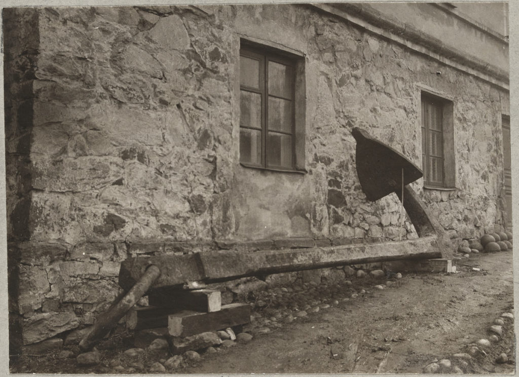 Svartvit bild av stort ankare placerat framför Kommendantshuset.