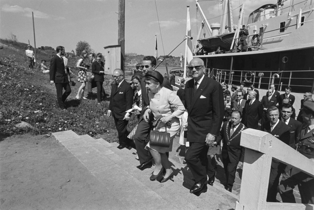 Elegant klädda herrar och damer stiger i land från en stor båt, utomhusbild i sommarväder.