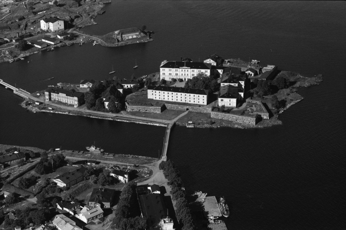 Flygbild av bebyggs ö som har broförbindelse åt två håll. Svartvit bild.