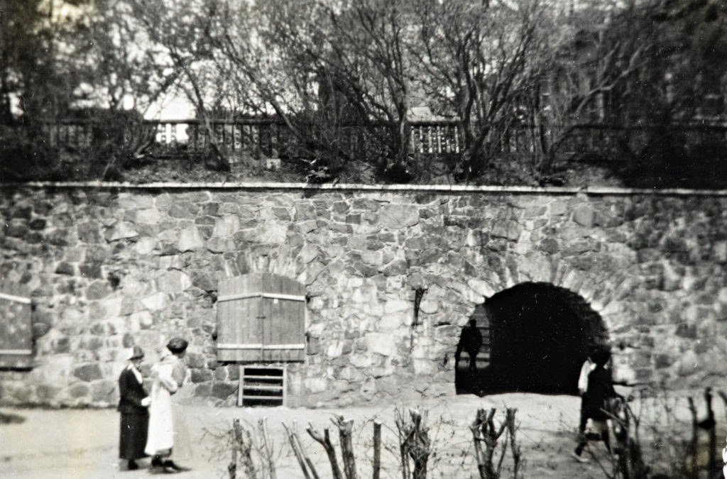 Två människor i parkmiljö, i bakgrunden en mur och träd.