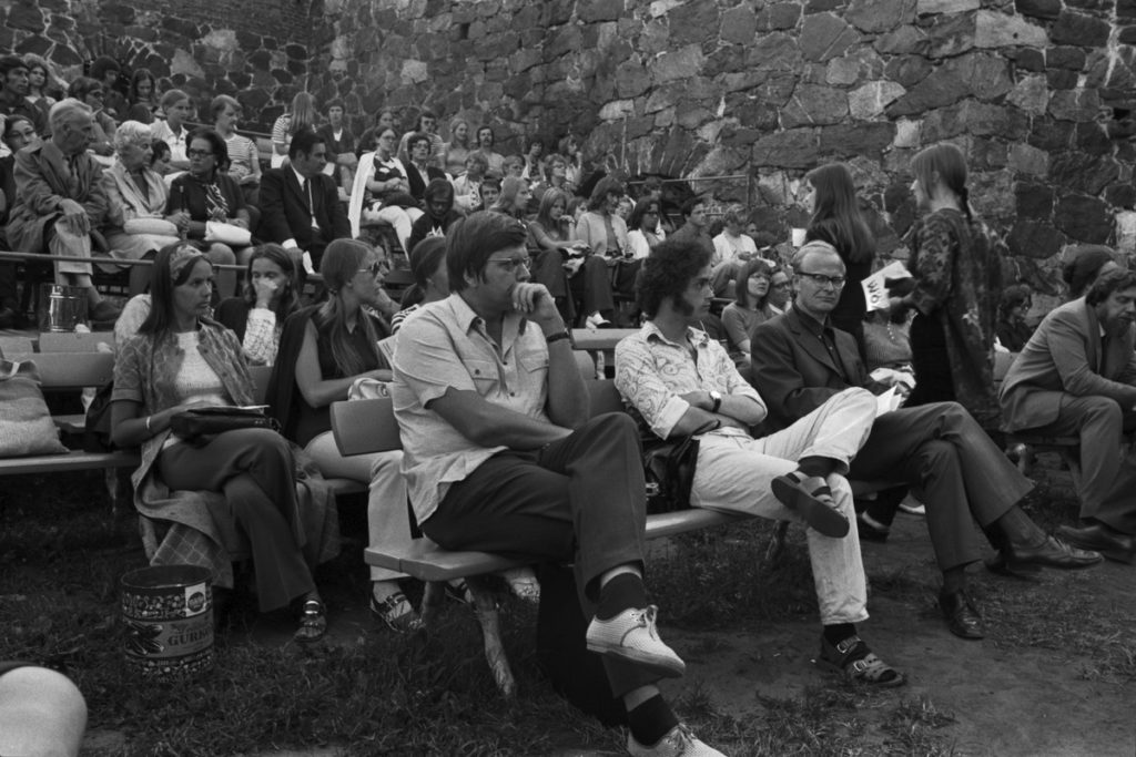 Många människor sitter utomhus och ser på något som sker utanför bilden.