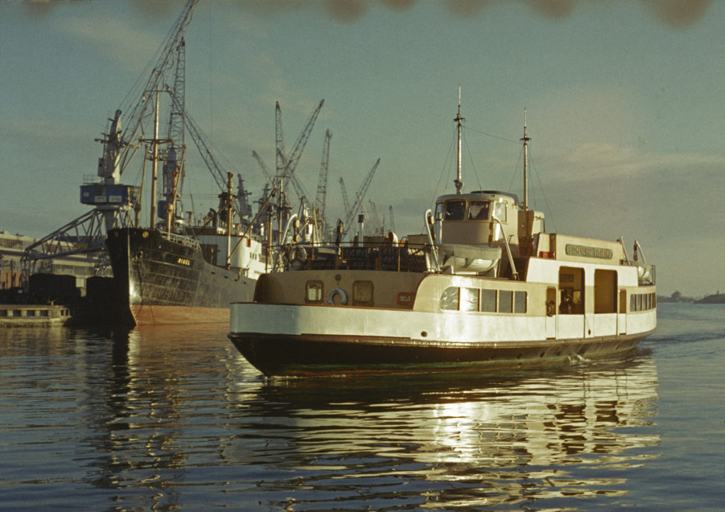 En passagerarfärja anländer till staden. Lyftkranar i bakgrunden.