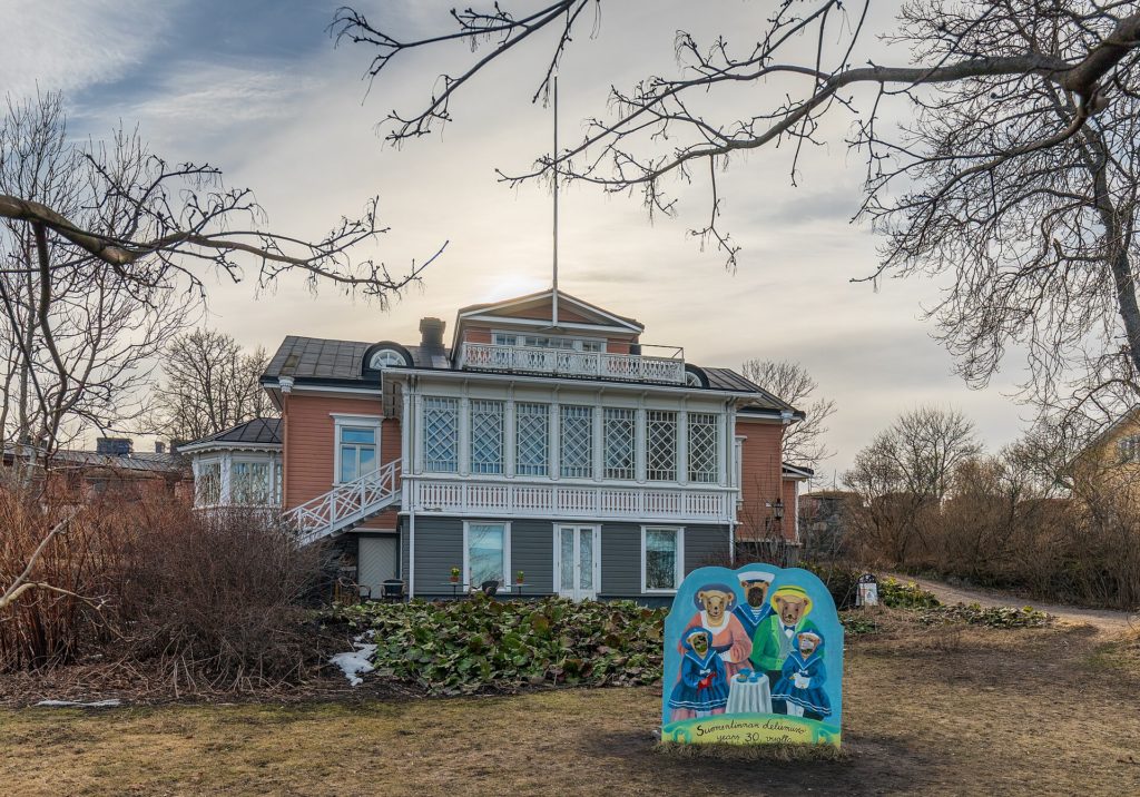 Trävilla med veranda i milt kvällssken tidigt på våren. Rosa hus, kvistar utan löv.